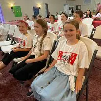 Children sitting in chairs, wearing matching shirts.