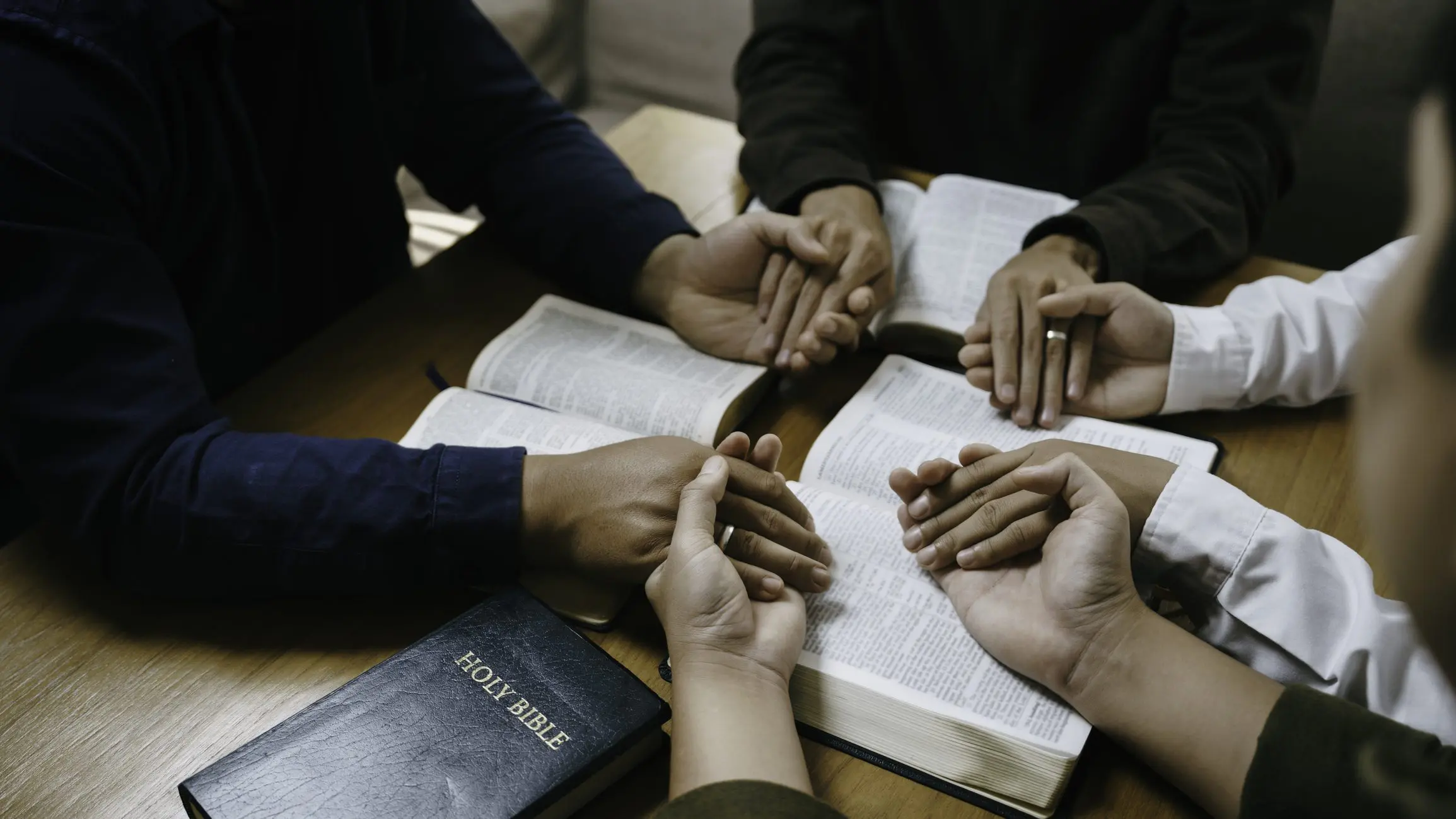 Hands holding in prayer over open Bible.