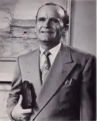 Man in suit holding a book, smiling.