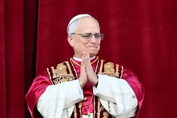 Religious leader in red robe, hands clasped.