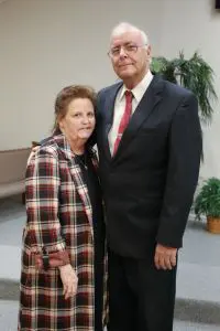 Elderly couple standing together, dressed formally.