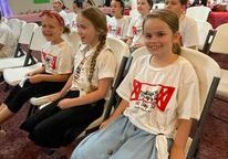 Children sitting in chairs, wearing matching shirts.