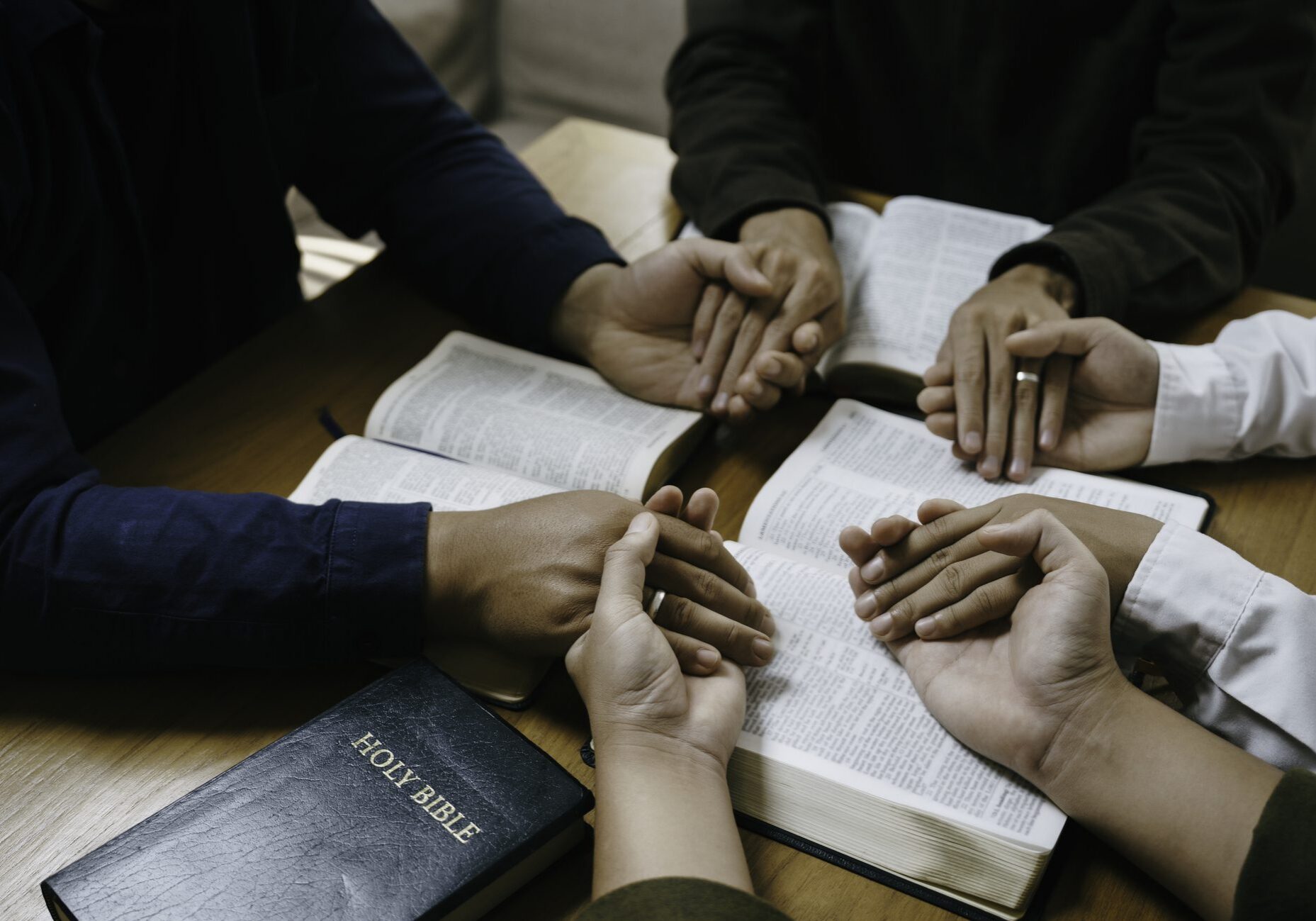 Hands holding in prayer over open Bible.