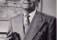 Man in suit holding a book, smiling.